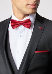 Black suit with a white shirt, featuring a red satin bow tie and a red pocket square. Notable lapel pin with a heart design.