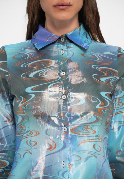 Camisa de botão em tons de azul com padrões ondulados em laranja e branco. Apresenta um colarinho e textura brilhante, feita de tecido leve.
