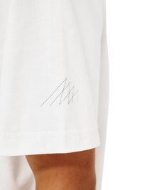 Weißes Kurzarmhemd mit kleinen schwarzen Zickzacknähten nahe am Saum über einem gebräunten Arm.