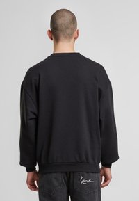 Sort sweatshirt med rund hals, løs pasform og ribstrikkede manchetter. Har en glat tekstur og et lille broderet logo på den nederste ryg.