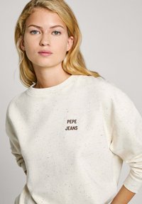 Grietos spalvos džemperis su taškinėmis tekstūromis, apvalia iškirpte ir išsiuvinėtu "PEPE JEANS" logotipu ruda spalva priekyje.