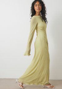 Abito a maniche lunghe, a coste, di un verde tenue, con silhouette aderente, scollo rotondo e polsini svasati. Indossato con sandali bianchi con cinturini.
