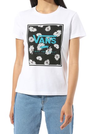 Kobieta nosząca białą koszulkę Vans z czarnym kwadratowym wzorem białych kwiatów, niebieskim logo Vans oraz motywem deskorolki.