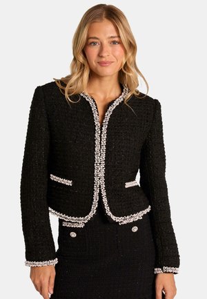 Giacca in tweed nera con una vestibilità su misura, rifinita con dettagli in perle lungo il colletto, le tasche e i polsini. Presenta maniche lunghe e un designCrop.