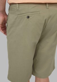 Olivgrüne Shorts aus leichtem Stoff, mit einer Rückentasche und einem schwarzen Knopf sowie einem geraden Schnitt.