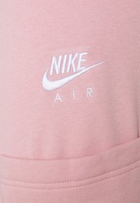 Rosa sweatshirtstoff med en slät textur, med vit broderad "Nike Air"-logotyp och swoosh-design nära den övre delen.