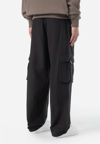 Black cargo pants made of lightweight fabric, featuring side pockets, a relaxed fit, and a smooth texture, paired with white sneakers.