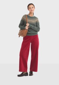 Knit green sweater with a Fair Isle pattern, red corduroy wide-leg pants, and brown leather crossbody bag. Deep brown shoes complete the look.