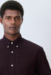 Dunkelviolette Button-Up-Hemd mit Kragen, ausgestattet mit weißen Knöpfen, einer Brusttasche und einem strukturierten Stoff. Einfaches Design, taillierte Passform.