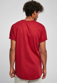 Tricou din bumbac roșu cu hem rotunjit și mâneci răsucite, prezentat din spate. Are o textură netedă și o croială lejeră.