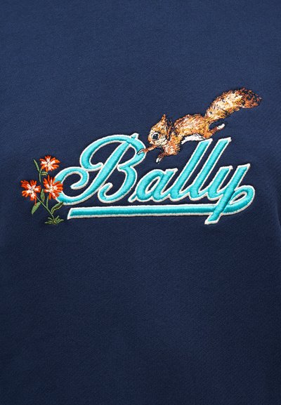 Ναυτικό ύφασμα με κεντημένο το "Bally" σε τιρκουάζ, συνοδευόμενο από σκίουρο και λουλούδια σε πορτοκαλί και πράσινο, προσθέτοντας υφή και λεπτομέρεια.