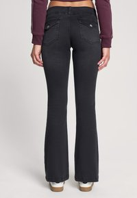 Czarne jeansy z szeroką nogawką o gładkiej fakturze, z dwoma tylnymi kieszeniami i srebrnymi detalami. Pas usytuowany jest wysoko, co pozwala uzyskać dopasowaną sylwetkę.