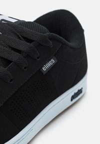 Baskets noires avec un dessus texturé, présentant des accents perforés sur les côtés. Logo blanc sur la languette, semelle bleu clair avec une traction en caoutchouc.