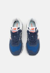 Une paire de baskets New Balance 574 bleu marine avec des détails blancs et orange, vue de dessus sur un fond blanc.