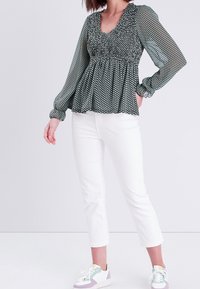 Blouse à motifs noir et blanc avec manches bouffantes, corsage froncé et encolure en V. Associée à un pantalon blanc coupé court et des baskets multicolores.