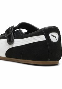 Μαύρο-άσπρο καθημερινό παπούτσι Puma με λουρί με πόρπη, σουέντ υφή, λευκή ραμμένη ρίγα στο πλάι και λογότυπο Puma στην κνήμη της φτέρνας.