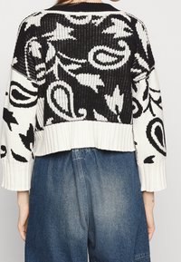 Krótki sweter dzianinowy w czarno-białym kolorze, z wzorem paisley i prążkowaną fakturą. Długie rękawy z szerokimi ściągaczami.