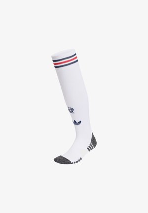 Biała skarpeta do kolan z czerwono-niebieskimi paskami na górze, ciemnoszarymi palcami i piętą oraz logo Adidas z napisem na łydce.