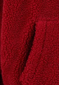 Gros plan d'un tissu polaire rouge profond, doux et bouclé avec une surface texturée et moelleuse.