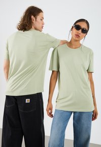 Light green cotton t-shirts with short sleeves, relaxed fit, and crew neck. Worn with black baggy pants and blue jeans.