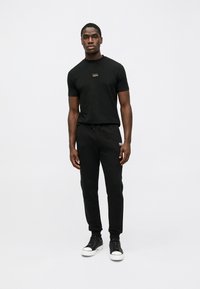 Μαύρο κοντομάνικο μπλουζάκι με μικρό λογότυπο, συνδυασμένο με μαύρες φόρμες που διαθέτουν ελαστική μέση και διακριτική επωνυμία; ολοκληρωμένο με μαύρα αθλητικά παπούτσια.