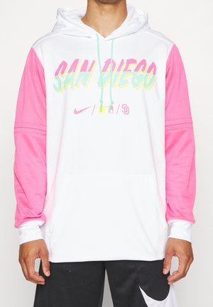 Mężczyzna ubrany w biały kaptur z różowymi rękawami i pastelowym napisem „San Diego”, w połączeniu z czarnymi szortami z białym logo Nike.