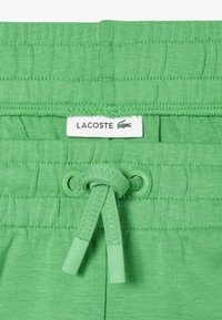 Gröna bomullsshorts med en texturerad midja och en justerbar snörning. Lacoste-logotypen sydd framtill.