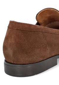 Brązowe zamszowe mokasyny o miękkiej teksturze, z zaokrąglonym obcasem i kontrastującą czarną gumową podeszwą. Minimalne detale szwów.