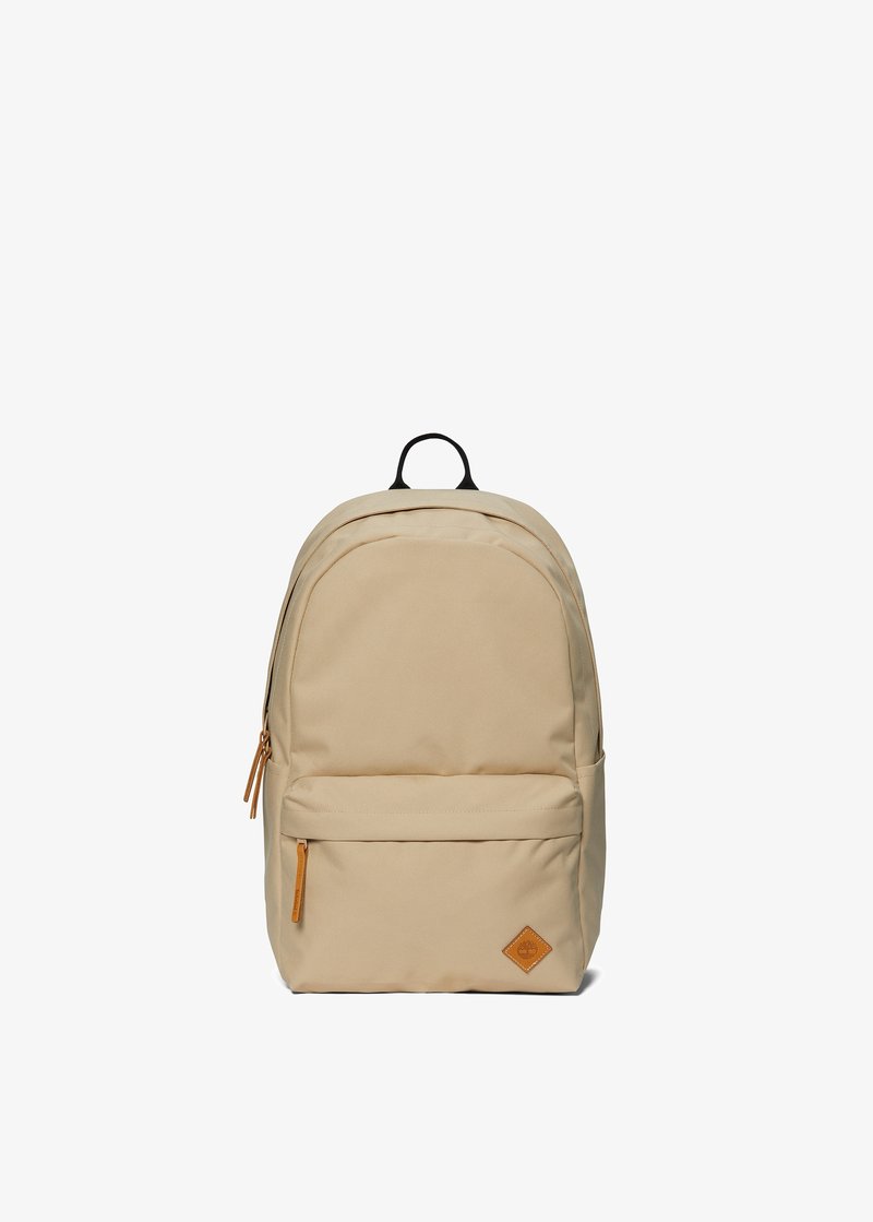 Sac à dos beige avec une surface en tissu lisse, une poche avant zippée et un accent en cuir en bas. Poignée supérieure noire pour le transport.