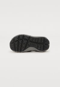 Suela de zapato de goma negra con un patrón de agarre texturizado. El diseño presenta un perfil plano y un logotipo elevado en el centro.