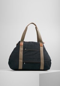 Sac fourre-tout en tissu noir avec de larges poignées beiges et une poche zippée à l'avant, exposé sur un piédestal blanc devant un fond gris.