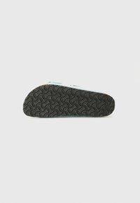 Semelle de chaussure avec une bande de roulement en caoutchouc noir texturé affichant un motif circulaire ondulé, vue par le dessous sur un fond uni.