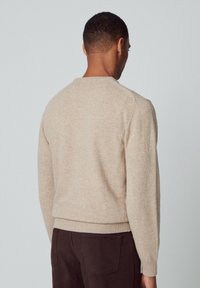 Beige knit sweater with a round neckline, ribbed hem, and long sleeves, displayed from the back. Cotton blend material, soft texture.