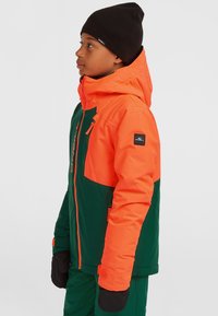 Kleurijke geïsoleerde skijas met een oranje bovenstuk en een groene onderkant, voorzien van een capuchon, ritsen en zwarte accenten.