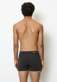 Boxer aderenti neri con una texture morbida e liscia. Presentano un cinturino elastico con logo. Visti da dietro, mostrano una copertura minima.