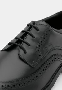 Pantofii negri din piele cu un finisaj neted, detalii brogue, sistem de închidere cu șireturi și vârf rotund. Caracterizează brandingul subtil pe lateral.