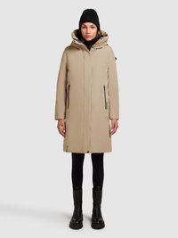 Beige isoleret frakke med hætte, sidelommer med lynlås og en lige pasform. Bruges over en sort rullekrave og leggings, kombineret med sorte kraftige støvler.