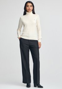 Dolcevita color avorio in un morbido e leggero tessuto a maglia, abbinato a pantaloni neri su misura e stivaletti neri con tacco.