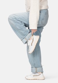 Sneaker atletiche bianche con accenti dorati, dettagli in rete e suola testurizzata. Indossate con jeans azzurri arrotolati e un maglione bianco peloso.