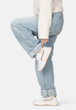 Weiße Sportsneaker mit goldfarbenen Akzenten, Mesh-Details und einer strukturierten Sohle. Getragen mit hochgekrempelten hellblauen Jeans und einem flauschigen weißen Pullover.
