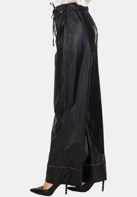 Pantaloni ampi in ecopelle nera con vita elasticizzata, chiusura con coulisse e cuciture a contrasto sull'orlo.