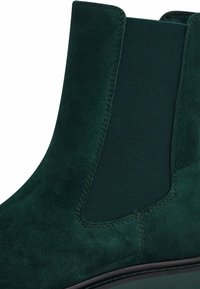 Bottine en daim vert foncé avec panneaux latéraux élastiques, bout arrondi et finition lisse. Détails couturés le long des bords.