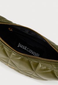 Olivnozeleno prešito sintetično usnjeno skladovnico z zlatim zadrgo, s črnim notranjim delom in vidno oznako logotipa.