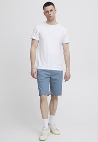White cotton t-shirt, blue shorts, and white sneakers with gray accents. Model stands on a light background, hands at sides.