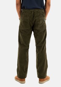 Pantaloni in corduroy di colore verde scuro con vestibilità rilassata, dotati di due tasche posteriori e una cintura elastica. Indossati con calzature color beige.