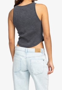 Femme portant un haut sans manches côtelé de couleur gris foncé et un jean en denim bleu clair avec des poches arrière et une étiquette en cuir sur la ceinture.