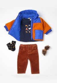 Tenue d'extérieur colorée comprenant une veste polaire bleue et orange, un t-shirt marine avec un design graphique, un pantalon en velours côtelé marron et des chaussettes à motifs.