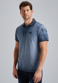 Polo da uomo in un colore blu sfumato. Realizzato in tessuto morbido, con collettobottonato, maniche corte e una tasca laterale con dettaglio del logo.