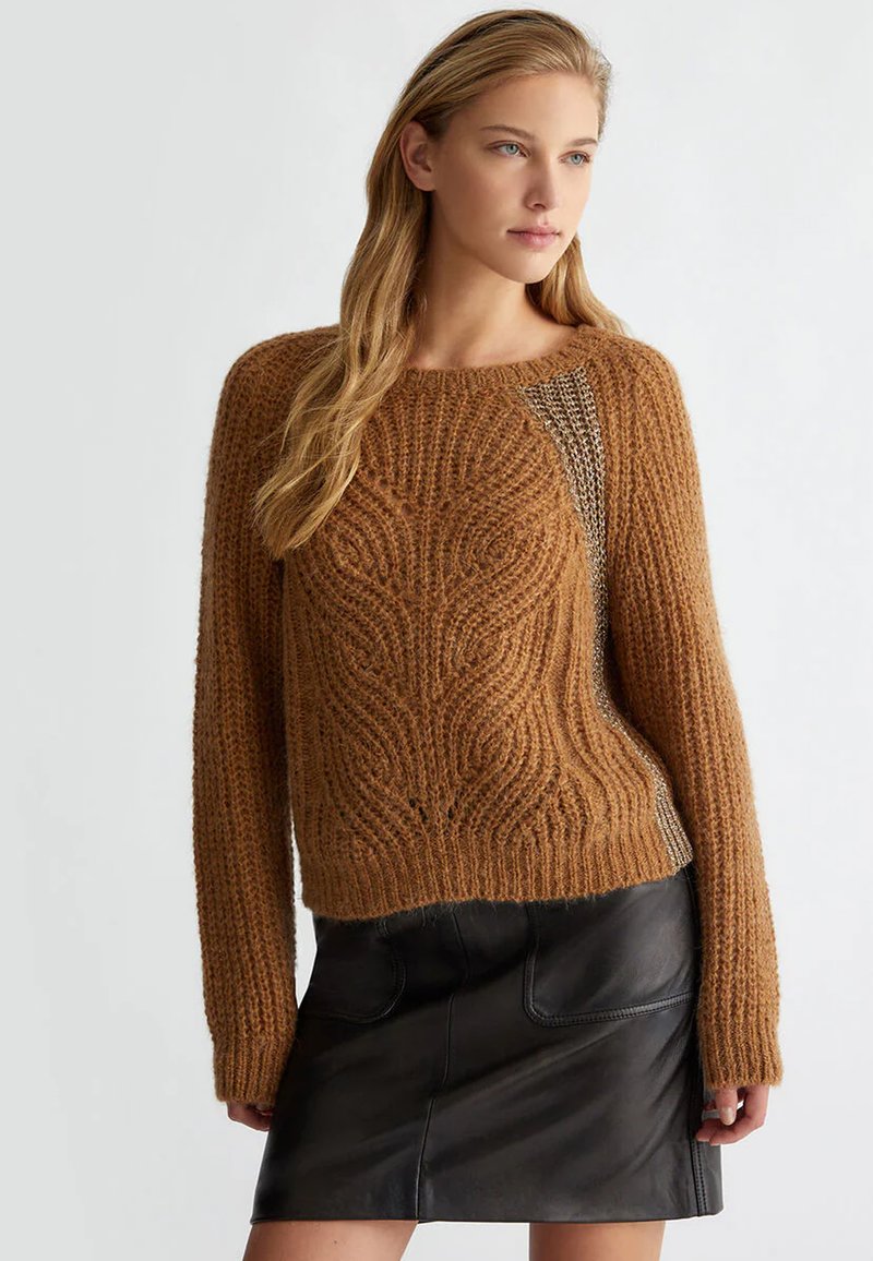 Maglione marrone lavorato a maglia con un motivo testurizzato e maniche ampie, abbinato a una gonna di pelle nera con tasche frontali.