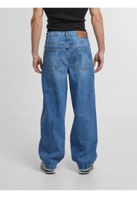 Jean en denim bleu à jambes larges avec taille haute, design à cinq poches et patch en cuir à la taille arrière. Texture douce, délavage. 